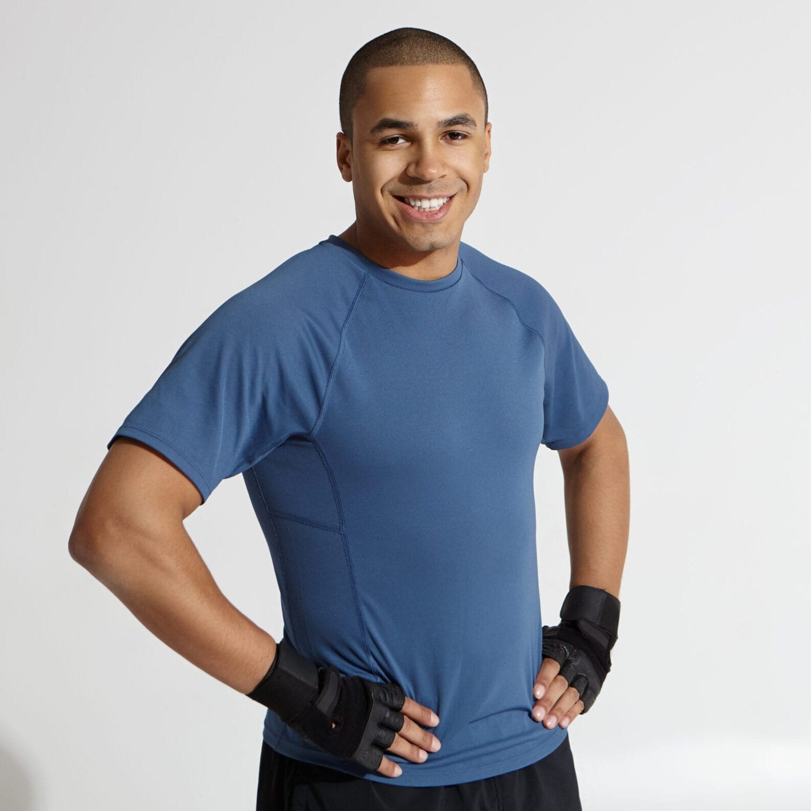 Cropped shot of happy young Afro American bodybuilder looking at camera and grinning confidently, keeping hands on his waist, posing against white studio wall background with copy space for your text