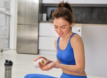 Image of young woman, sporty fitness girl taking vitamins, dietary supplements for muscles strength, sitting on yoga mat and workout.